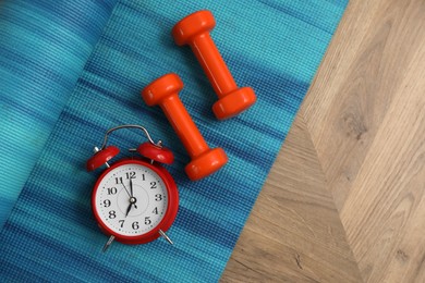 Alarm clock, yoga mat and dumbbells on wooden background, flat lay. Morning exercise