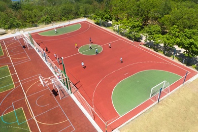 Children playing soccer at outdoor sports complex on sunny day, aerial view
