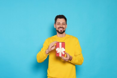 Photo of Happy man with gift box on light blue background