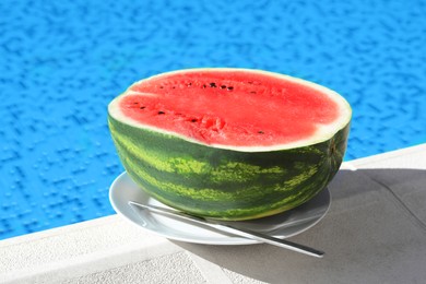 Half of fresh juicy watermelon on white plate near swimming pool outdoors