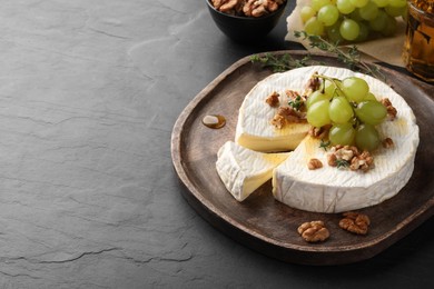 Photo of Brie cheese served with grapes, walnuts and honey on grey table. Space for text