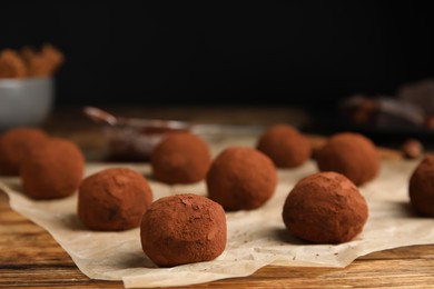 Delicious chocolate truffles powdered with cocoa on wooden table, closeup. Space for text