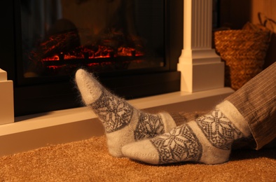 Photo of Woman in warm socks sitting near fireplace with burning wood at home, closeup