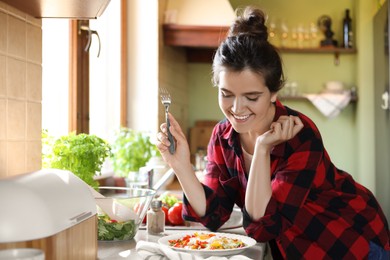 Young woman with plate of freshly fried eggs and vegetables at countertop in kitchen