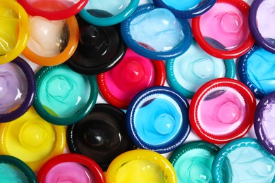 Unpacked colorful condoms as background, top view. Safe sex