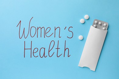Photo of Words Women's Health and pills on light blue background, flat lay