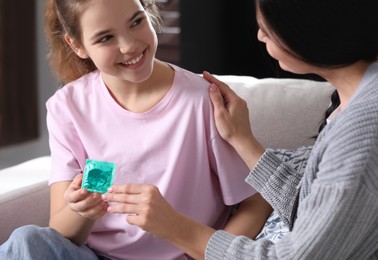 Mother giving condom to her teenage daughter at home. Sex education concept