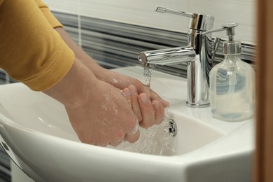 Man using water tap to rinse soap off hands in bathroom, closeup