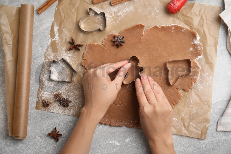 Photo of Woman making Christmas gingerbread cookies at grey table, top view