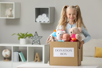 Cute little girl holding donation box with toys at home, space for text