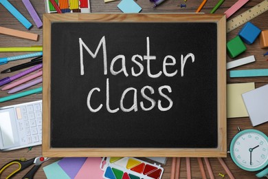 Photo of Blackboard with words Master Class surrounded by different stationery on wooden table, flat lay