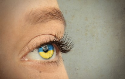 Young woman on light grey background, closeup view of eye with Ukrainian flag reflection