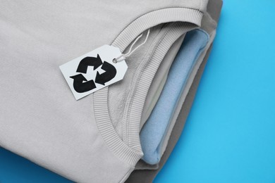 Stack of clothes with recycling label on light blue background, closeup
