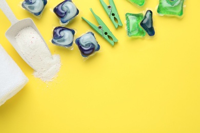 Different laundry capsules, washing powder and clothespins on yellow background, flat lay. Space for text