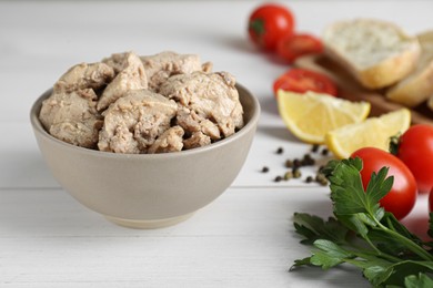 Photo of Bowl of tasty cod liver and different products on white wooden table, closeup