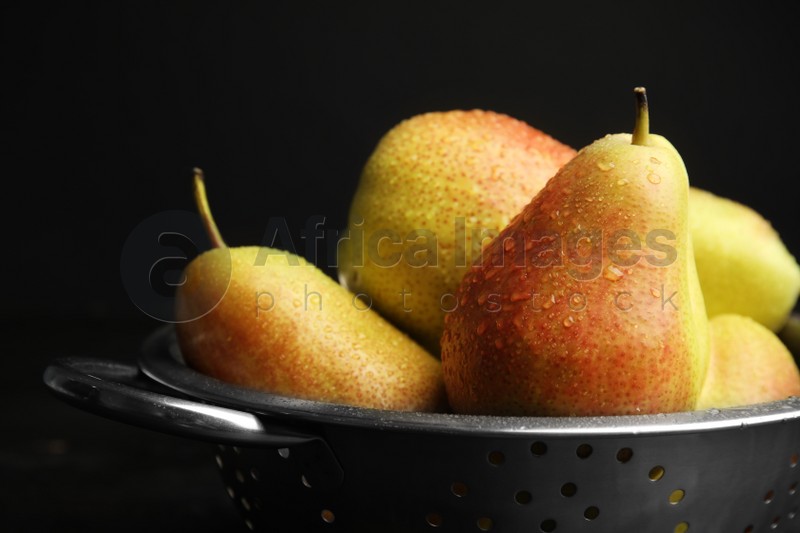 Colander with pears against black background, closeup