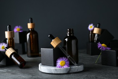 Bottles of essential oil and beautiful flowers on dark gray stone table