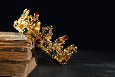 Beautiful golden crown and old books on black table, space for text. Fantasy item