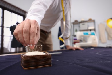 Tailor taking pin from cushion at table in workshop, closeup. Space for text