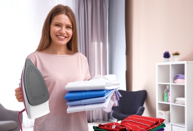 Young woman with folded clothes and iron at home. Space for text