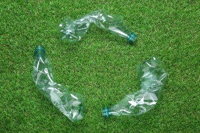 Recycling symbol made of crumpled plastic bottles on green grass, flat lay