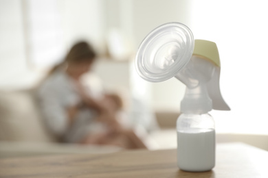 Mother feeding her little baby at home, focus on breast pump with milk. Healthy growth