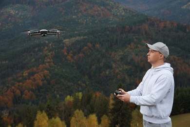 Young man operating modern drone with remote control in mountains, space for text