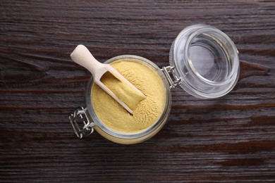 Photo of Scoop and glass jar with granulated brewer`s yeast on wooden table, top view