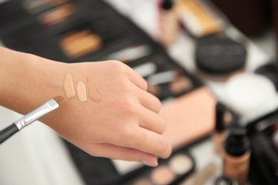 Woman testing different shades of liquid foundation on her hand against blurred background, closeup