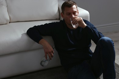Addicted man drinking alcohol near sofa indoors