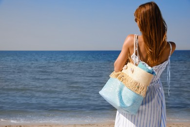 Woman with beach bag near sea, back view. Space for text