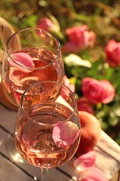 Photo of Glasses of delicious rose wine with petals on white picnic blanket outside, above view