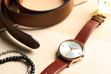 Luxury wrist watch, belt and bracelets on wooden background, closeup