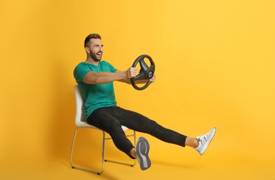 Happy man on chair with steering wheel against yellow background
