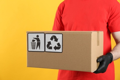 Courier holding cardboard box with different packaging symbols on yellow background, closeup. Parcel delivery