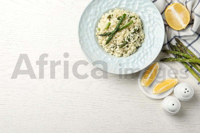 Delicious risotto with asparagus on white wooden table, flat lay. Space for text