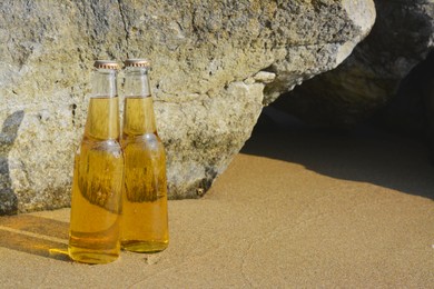 Bottles of cold beer near rock on sandy beach, space for text