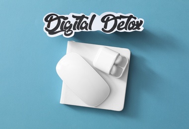 Paper note with phrase DIGITAL DETOX, mouse and earphones on light blue background, flat lay