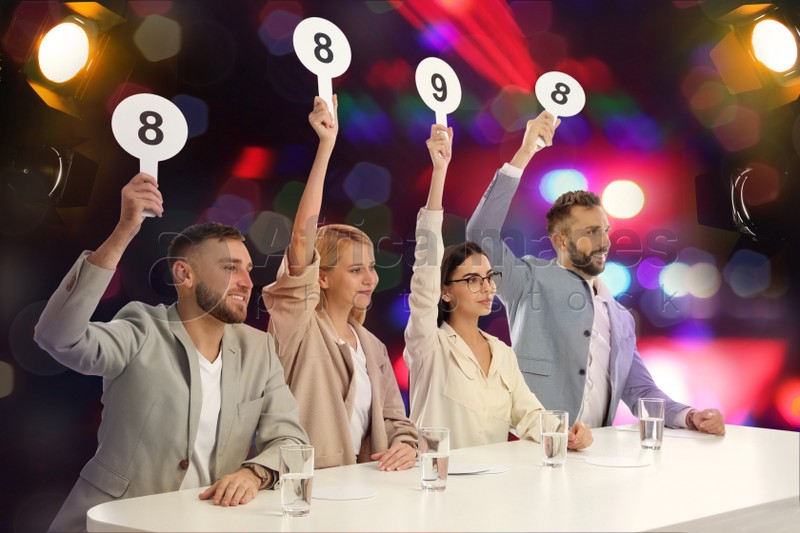 Panel of judges holding different score signs at table against blurred background. Bokeh effect