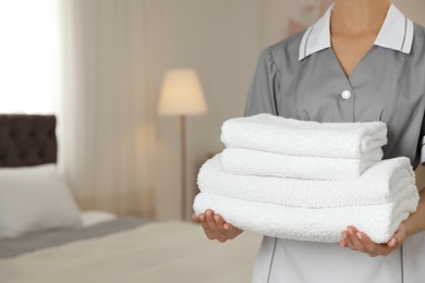 Chambermaid with stack of fresh towels in hotel room, closeup. Space for text