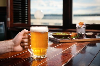 Man with glass of tasty beer at wooden table in pub, closeup. Space for text