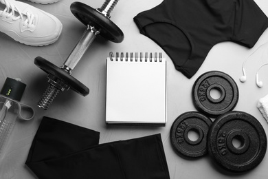 Flat lay composition with sportswear, notebook and equipment on grey table. Gym workout plan