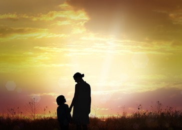 Silhouettes of godparent with child in field at sunrise
