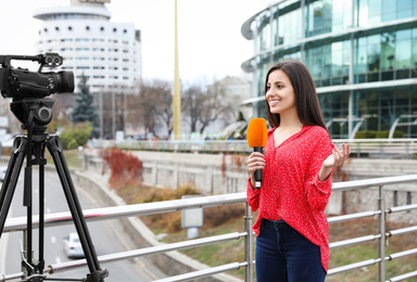 Young female journalist with microphone working on city street