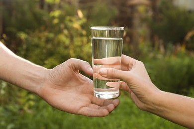 Woman giving glass of fresh water to man outdoors, closeup