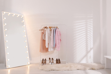Photo of Rack with stylish women's clothes and mirror indoors. Interior design