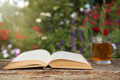Open book with glass cup of tea on wooden table in garden