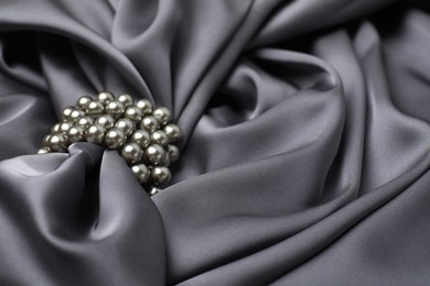 Beautiful pearls with grey silk as background, closeup. Space for text