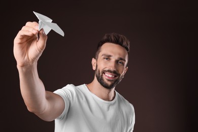 Handsome man playing with paper plane on brown background