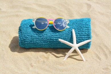 Photo of Towel, stylish sunglasses and starfish on sand outdoors. Beach accessories